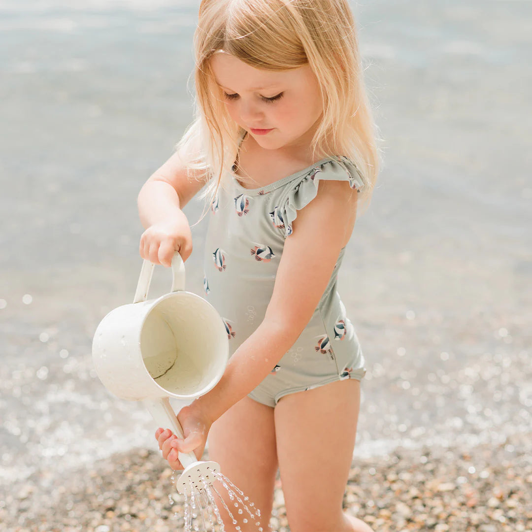 Baby girl playing at the beach in blue mist tropical fish kids swimsuit with flutter trims