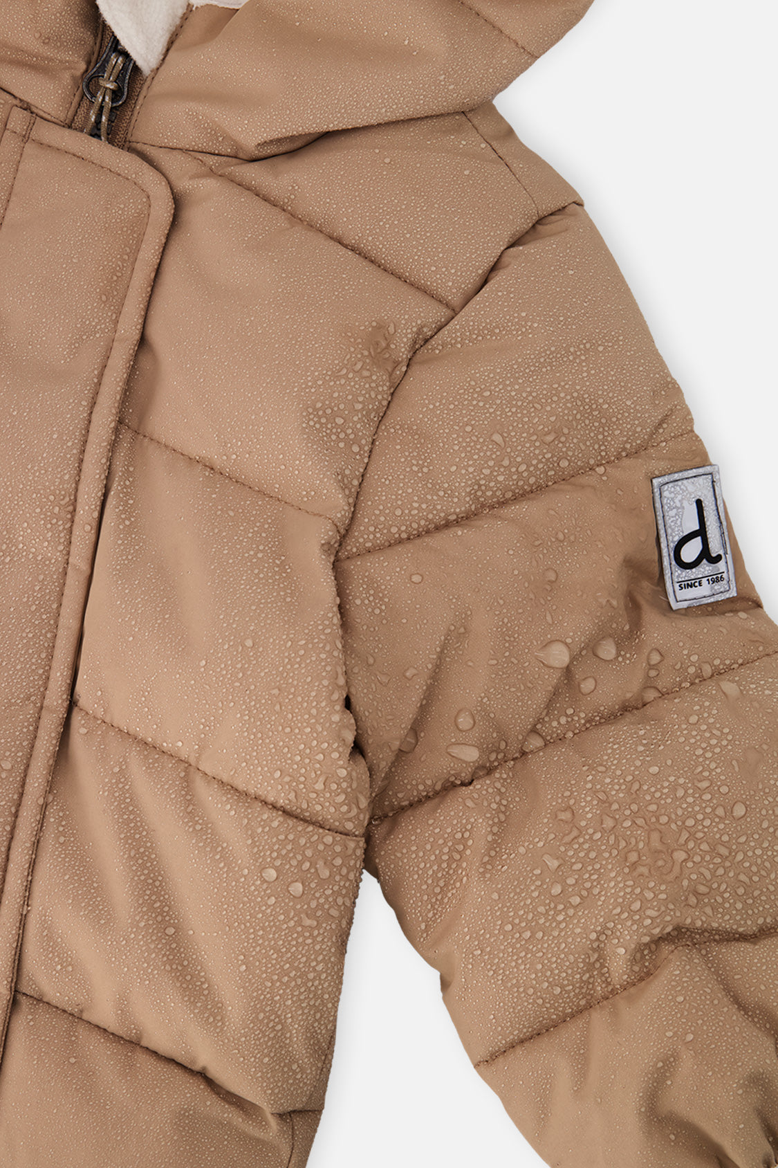 Close-up of the beige quilted sleeve with Deux par Deux logo patch