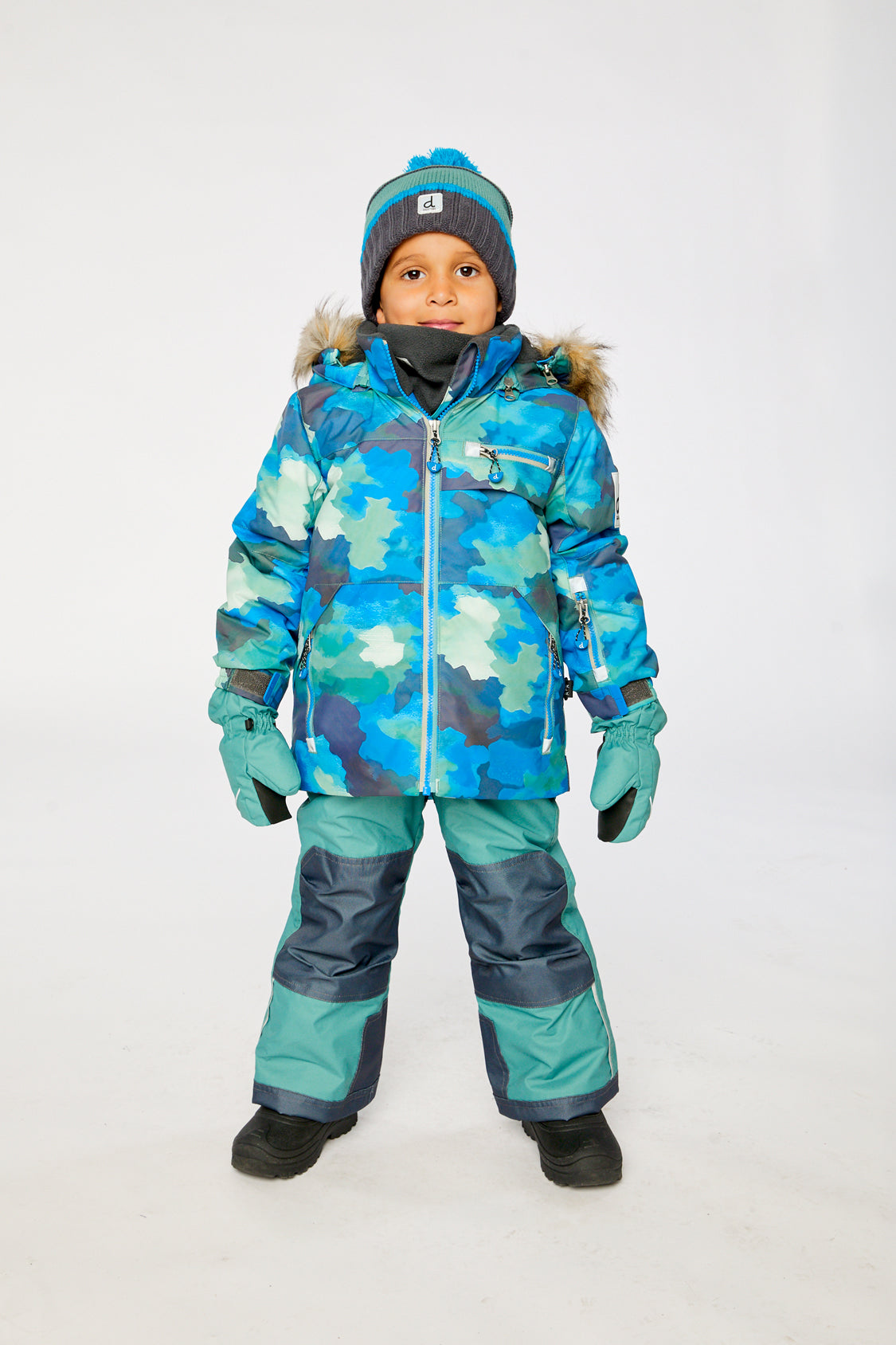 Boy wearing Deux par Deux blue camouflage PLAY snowsuit with green snow pants