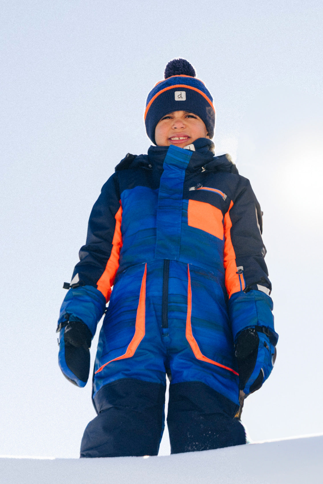 Child wearing the blue and black striped Deux par Deux PLAY snowsuit in an active winter lifestyle view