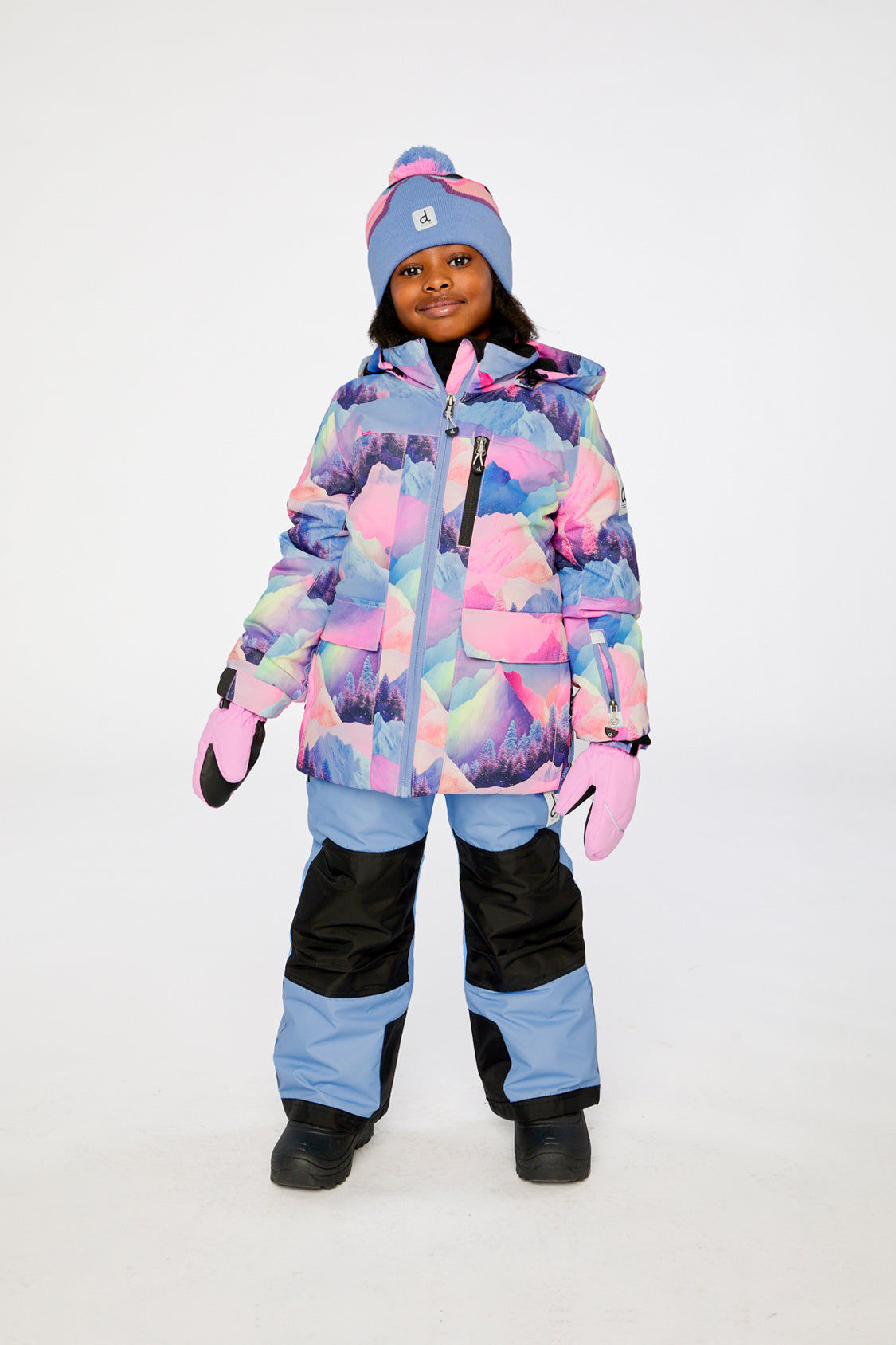 Child wearing the Deux par Deux PLAY two-piece snowsuit in Pink Mountain Print with Blue Pants in a winter lookbook view