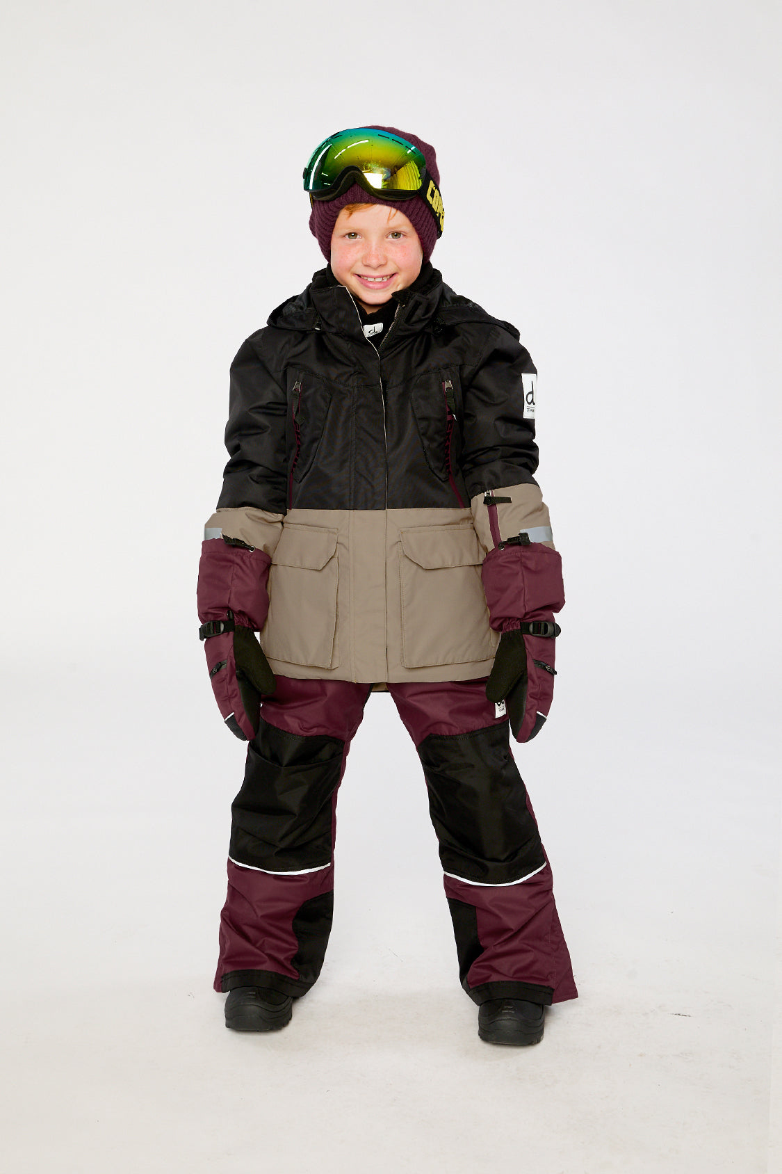 Child wearing the black, beige and burgundy Deux par Deux TEKNIK snowsuit in a winter lookbook view