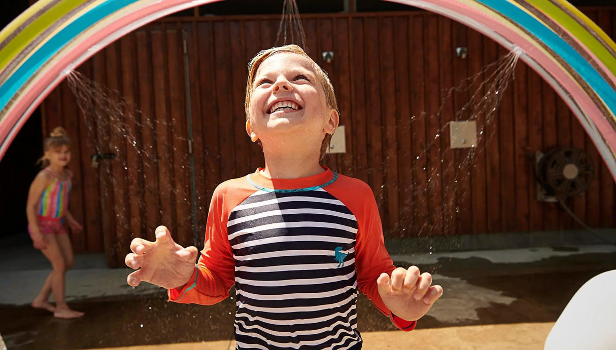 Kids wearing Hatley navy and orange dino rash guard top at splash pad