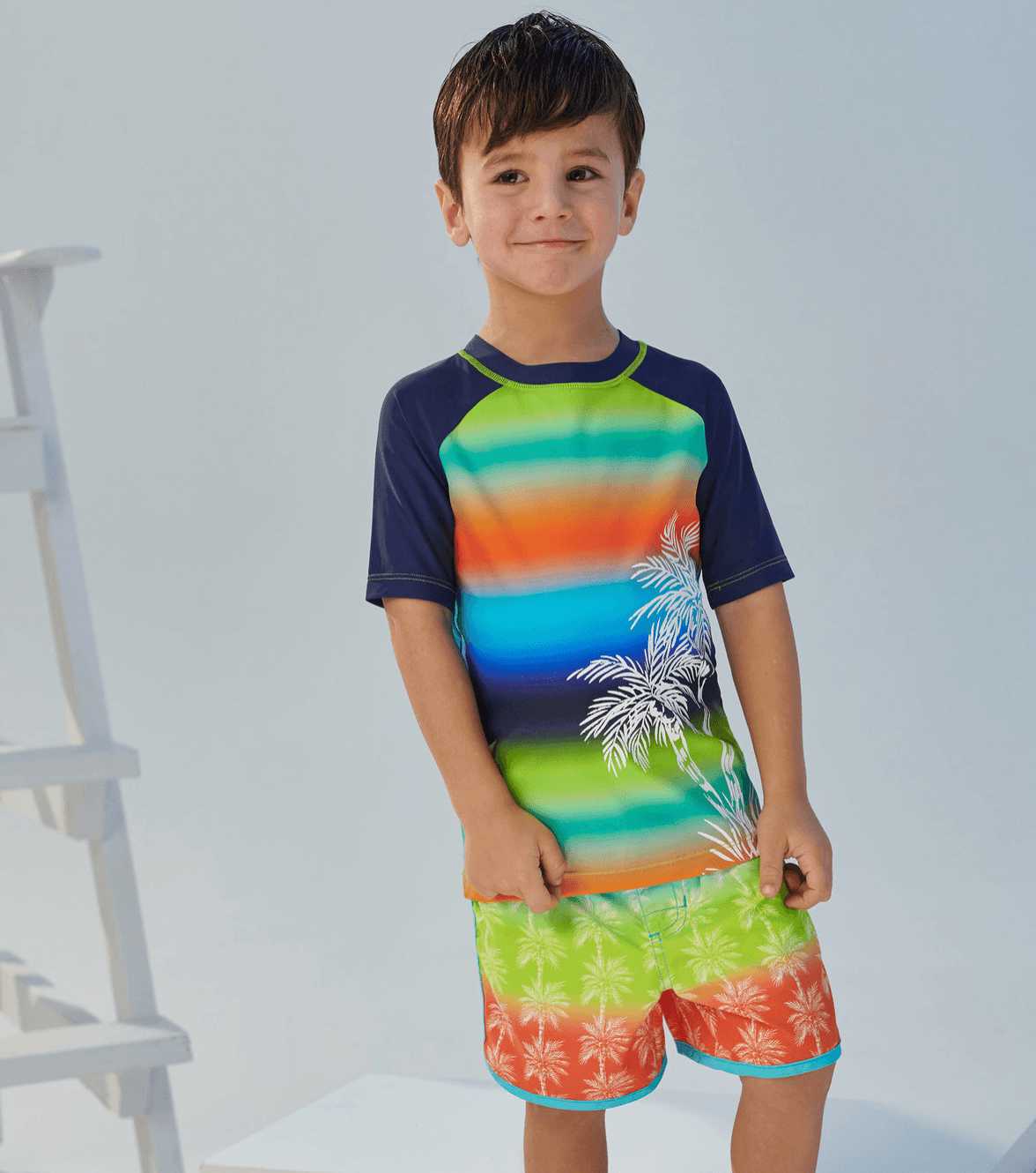 Boy wearing Hatley Gradient Palms rashguard with bright swim trunks