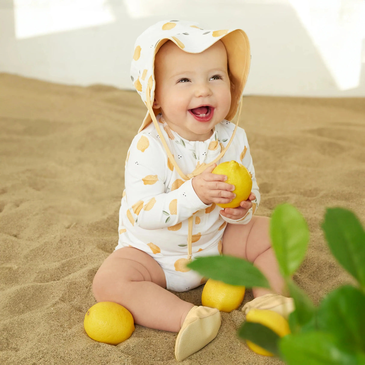 Baby playing in the sand wearing lemon-print long-sleeve rashguard set with matching hat.