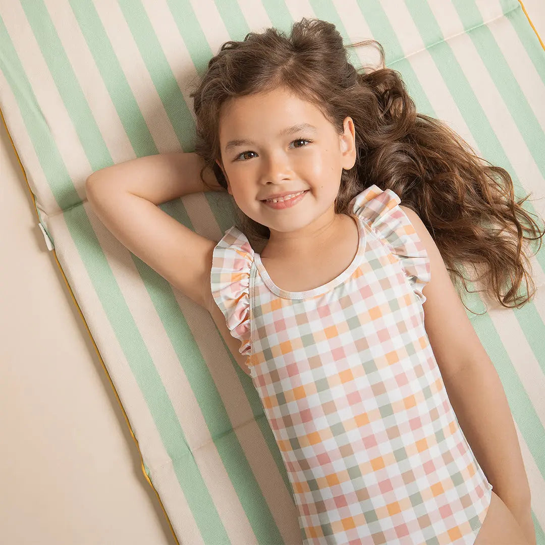 Child wearing pastel gingham one-piece swimsuit smiling on a summer day.