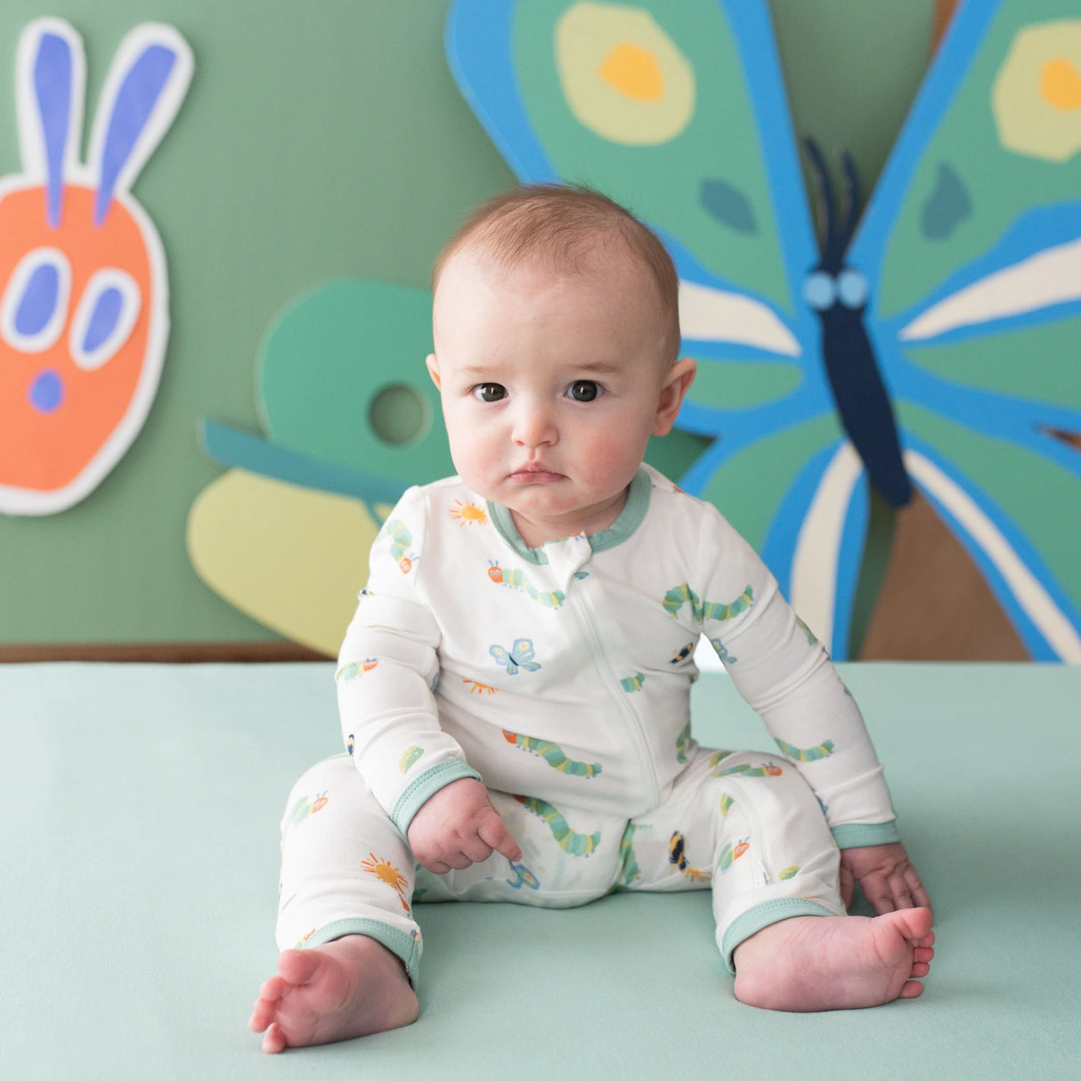 Baby sitting in Kyte Baby Caterpillar bamboo romper with playful wall art