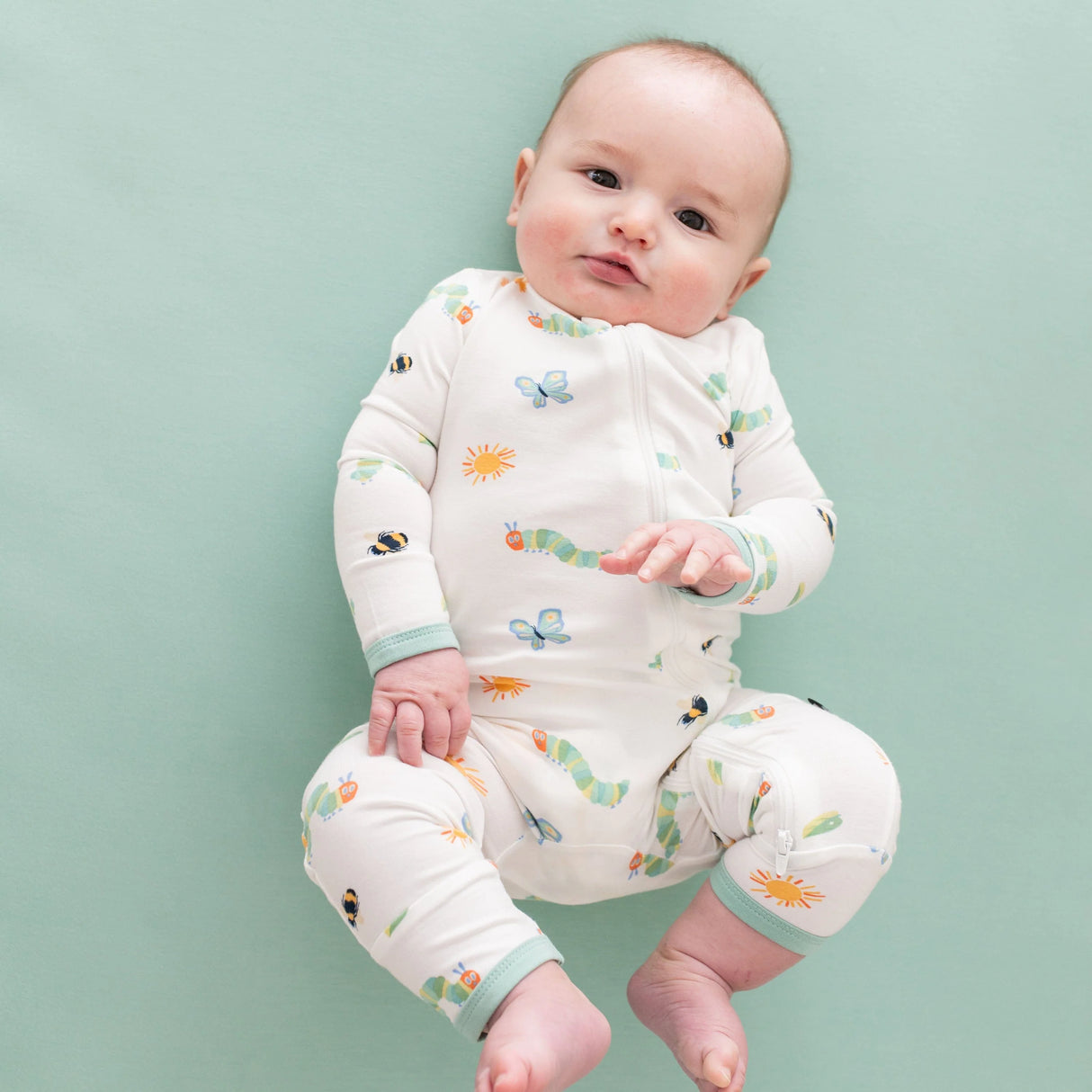 Baby wearing Kyte Baby Caterpillar zippered romper on soft green background