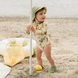 Baby girl wearing antique white citrus print long-sleeve swimsuit playing at the beach.