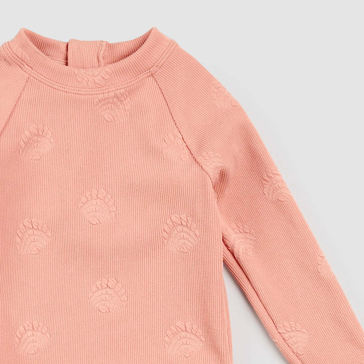 Close-up of embossed seashell ribbed texture on coral Petit Lem kids swimsuit rashguard top