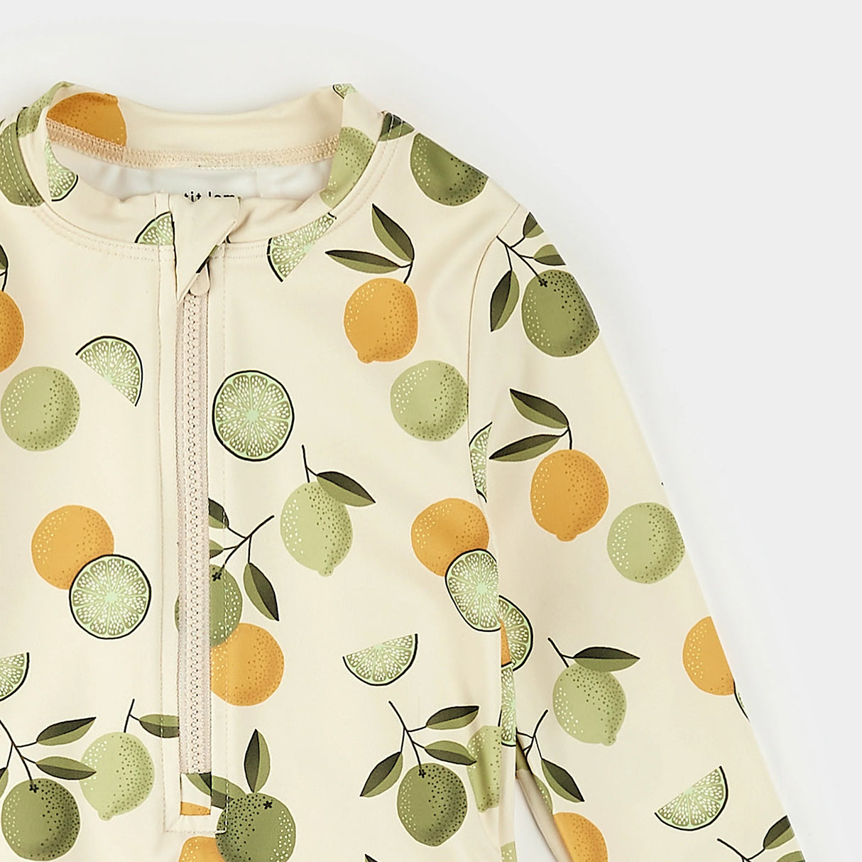 Close-up of citrus print fabric and frilly trim on Petit Lem long-sleeve kids swimsuit.