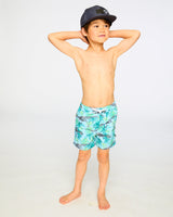 Boy standing with hands behind head showing front view of blue skeleton boardshorts
