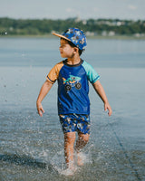 Boy playing in shallow water wearing blue truck boardshorts and matching swim top