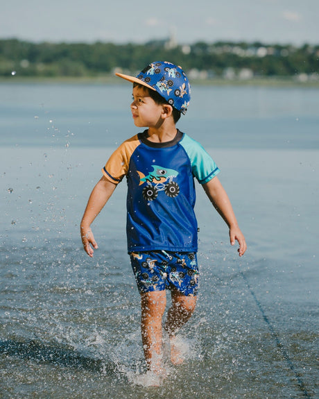 Boy playing in shallow water wearing blue truck boardshorts and matching swim top
