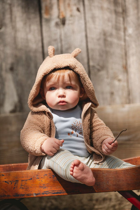Cute baby boy in beige teddy bear hoodie with ears, printed bodysuit and striped leggings – warm and stylish baby clothes at Jenni Kidz Canada.