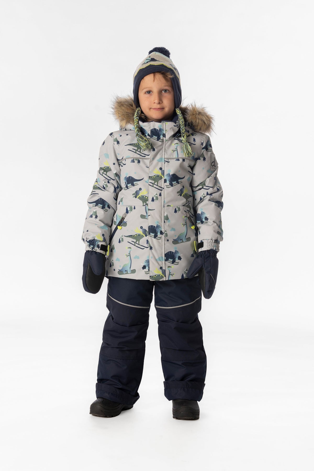 Boy standing in the grey dinosaur print Deux par Deux DISCOVER snowsuit, full-length front view