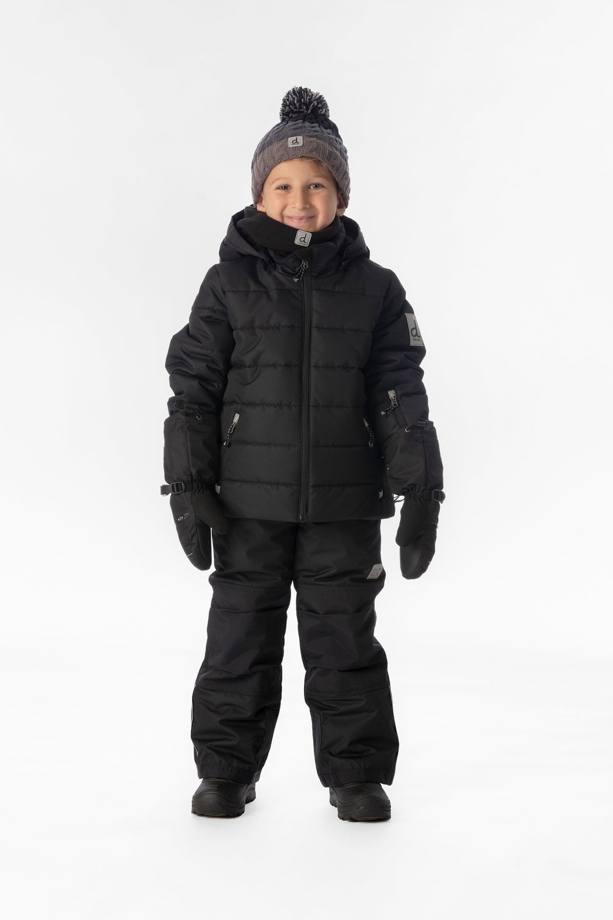 Boy standing in the all-black Deux par Deux PLAY snowsuit, full-length front view
