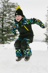 Boy wearing Deux par Deux checkerboard PLAY snowsuit jumping in snow