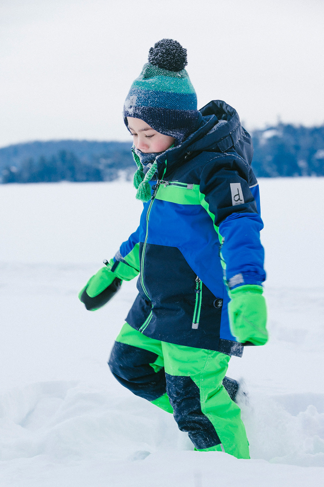 Deux par Deux PLAY two-piece snowsuit in Royal Blue and Green Colorblock shown in an alternate outdoor winter lifestyle view