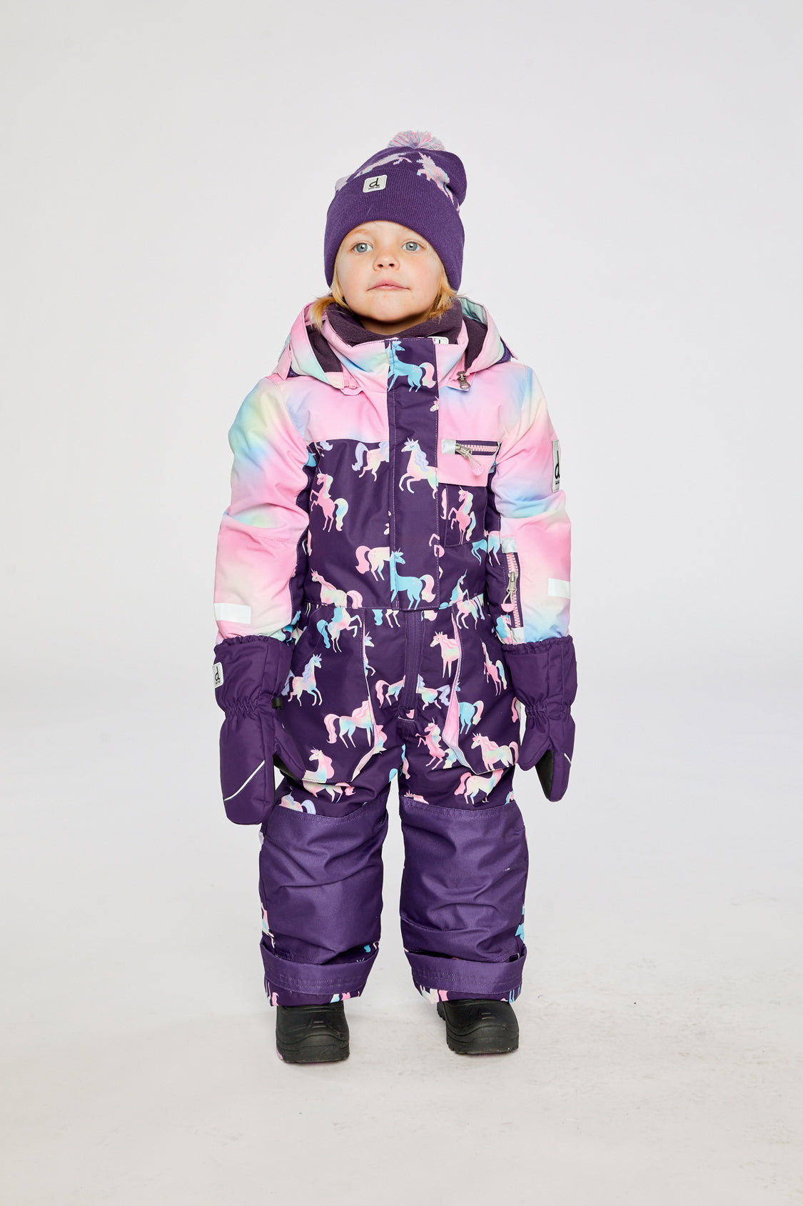 Child wearing the Deux par Deux kids PLAY one-piece snowsuit in Purple Unicorn Print in a winter lookbook view