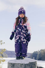 Child wearing the Deux par Deux kids PLAY one-piece snowsuit in Purple Unicorn Print during outdoor winter play