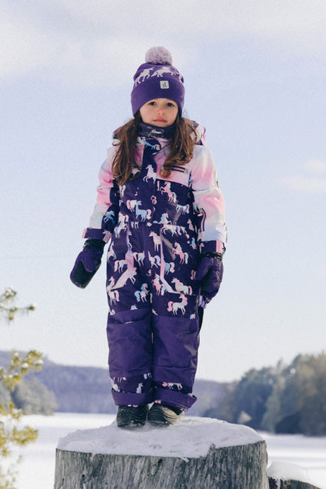 Child wearing the Deux par Deux kids PLAY one-piece snowsuit in Purple Unicorn Print during outdoor winter play