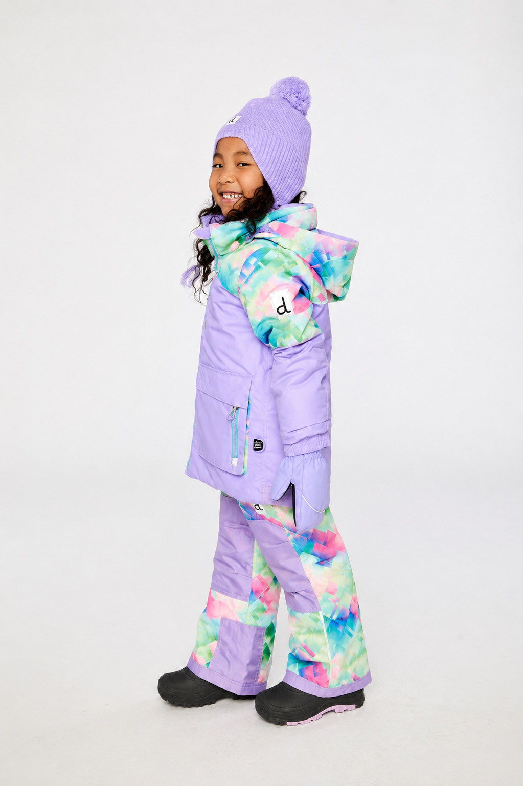 Side view of a child wearing the lavender and multicolor diamond-print snowsuit with a patterned hood
