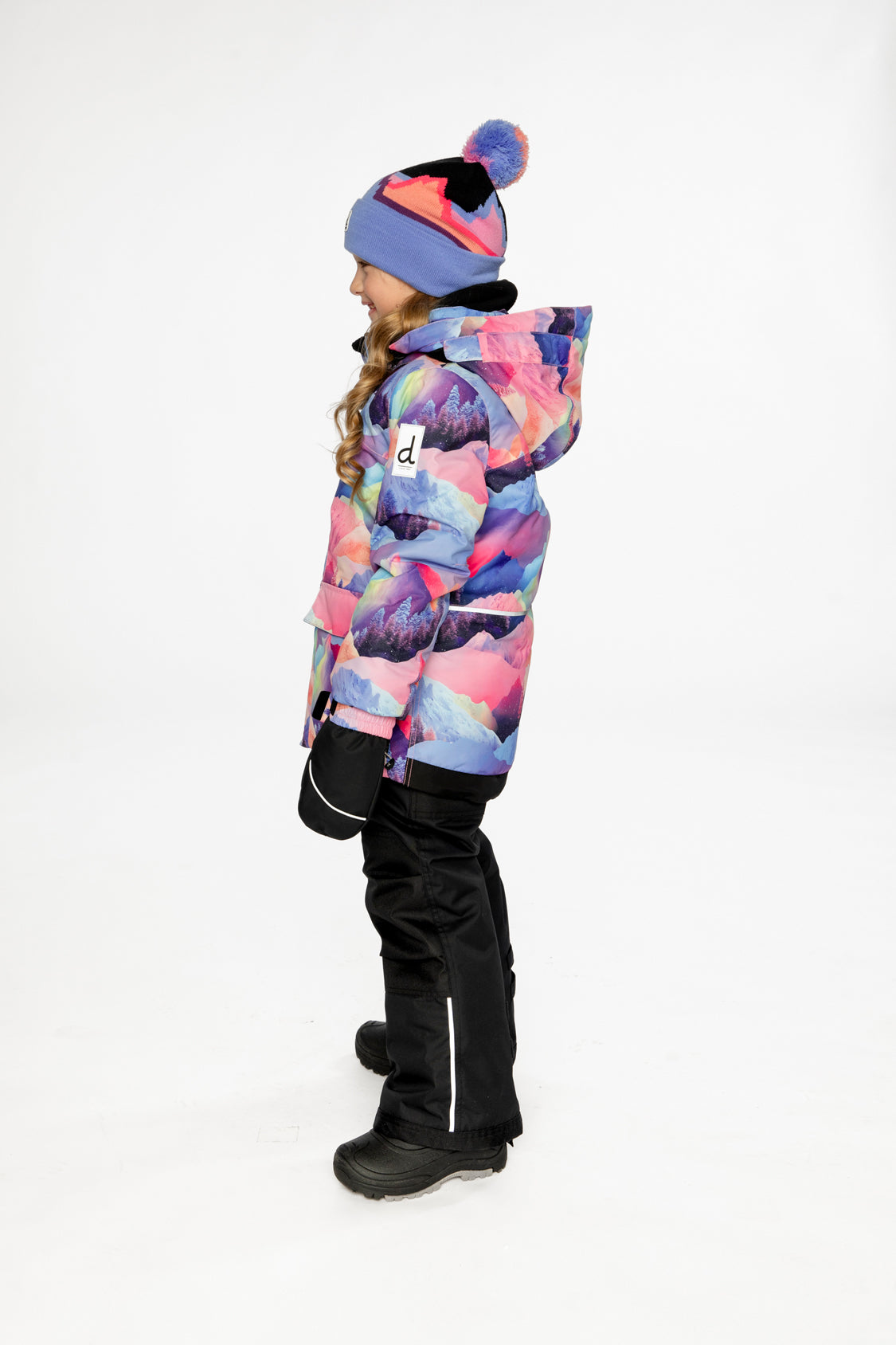 Side view of a child wearing the pink mountain-print snowsuit, showing the hood and black snow pants