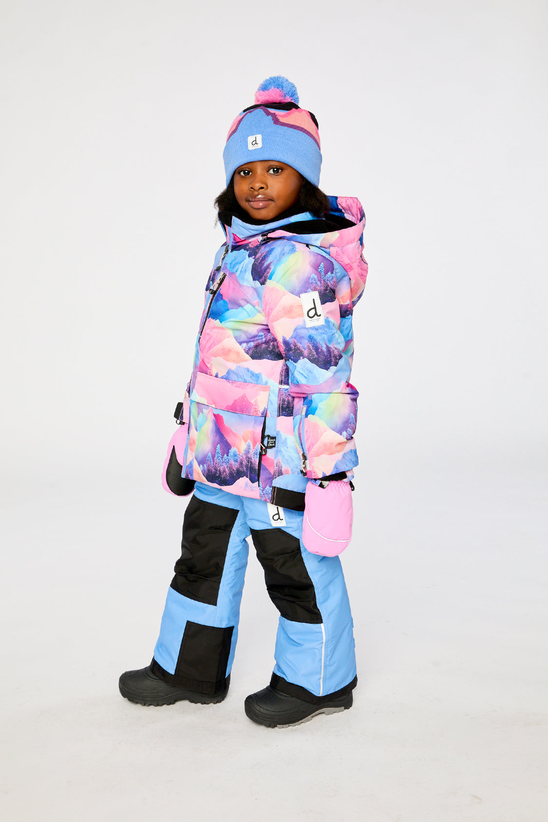 Deux par Deux PLAY two-piece snowsuit in Pink Mountain Print with Blue Pants shown from an alternate modeled winter angle