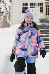 Child wearing the Deux par Deux PLAY two-piece snowsuit in Pink Mountain Print with Blue Pants during outdoor winter play