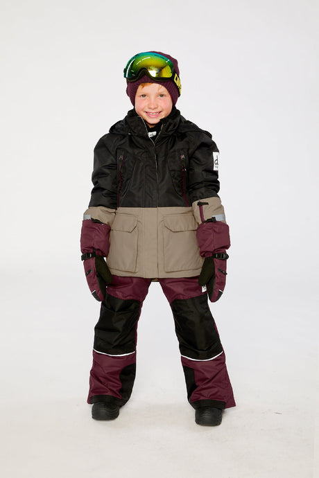 Child wearing the black, beige and burgundy Deux par Deux TEKNIK snowsuit in a winter lookbook view