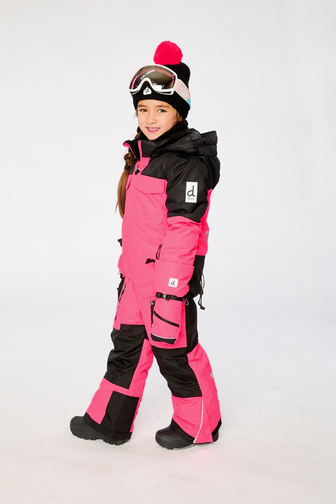 Deux par Deux kids TEKNIK one-piece snowsuit in Bright Pink shown from an alternate modeled winter angle