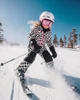 Girl skiing downhill in the checkered Deux par Deux TEKNIK snowsuit and a white helmet