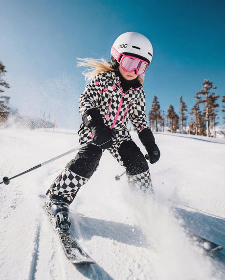 Girl skiing downhill in the checkered Deux par Deux TEKNIK snowsuit and a white helmet