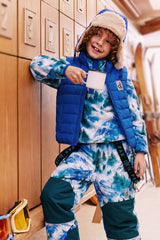 Boy standing in a ski lodge wearing the Deux par Deux blue lined chapka with a matching snow outfit