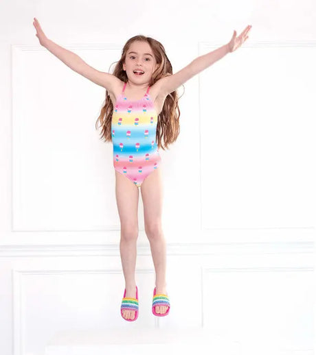 Girl jumping in Hatley Sweet Treats multicolor girls one-piece swimsuit with pastel stripes and treats print