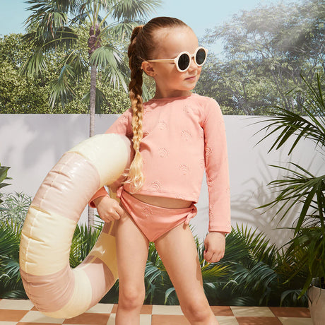 Lifestyle photo of girl wearing coral ribbed seashell rashguard swim set with long sleeves and matching bottoms