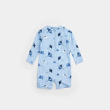 Baby girl wearing sky blue stingray print long-sleeve swim romper by Petit Lem at the beach