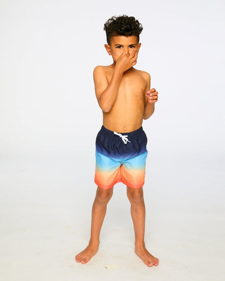 Boy standing in studio in blue/orange gradient swim trunks front view