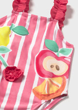 Closeup of Mayoral baby girl graphic swimsuit showing Pink stripes, ruffled strap, and colorful print.