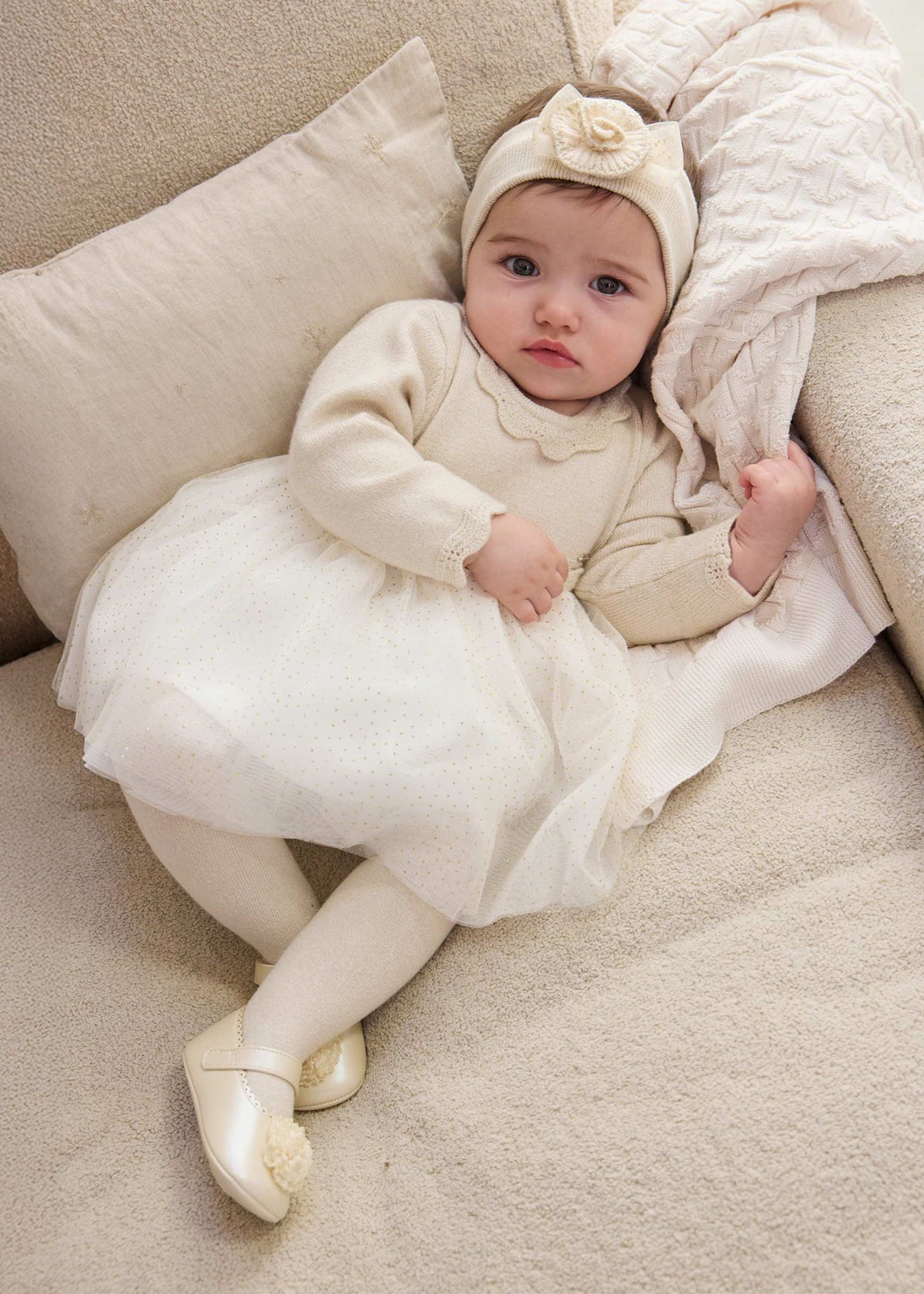 Baby wearing ivory Mayoral tulle dress with gold dots and a separate headband