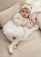 Baby wearing ivory Mayoral tulle dress with gold dots and a separate headband